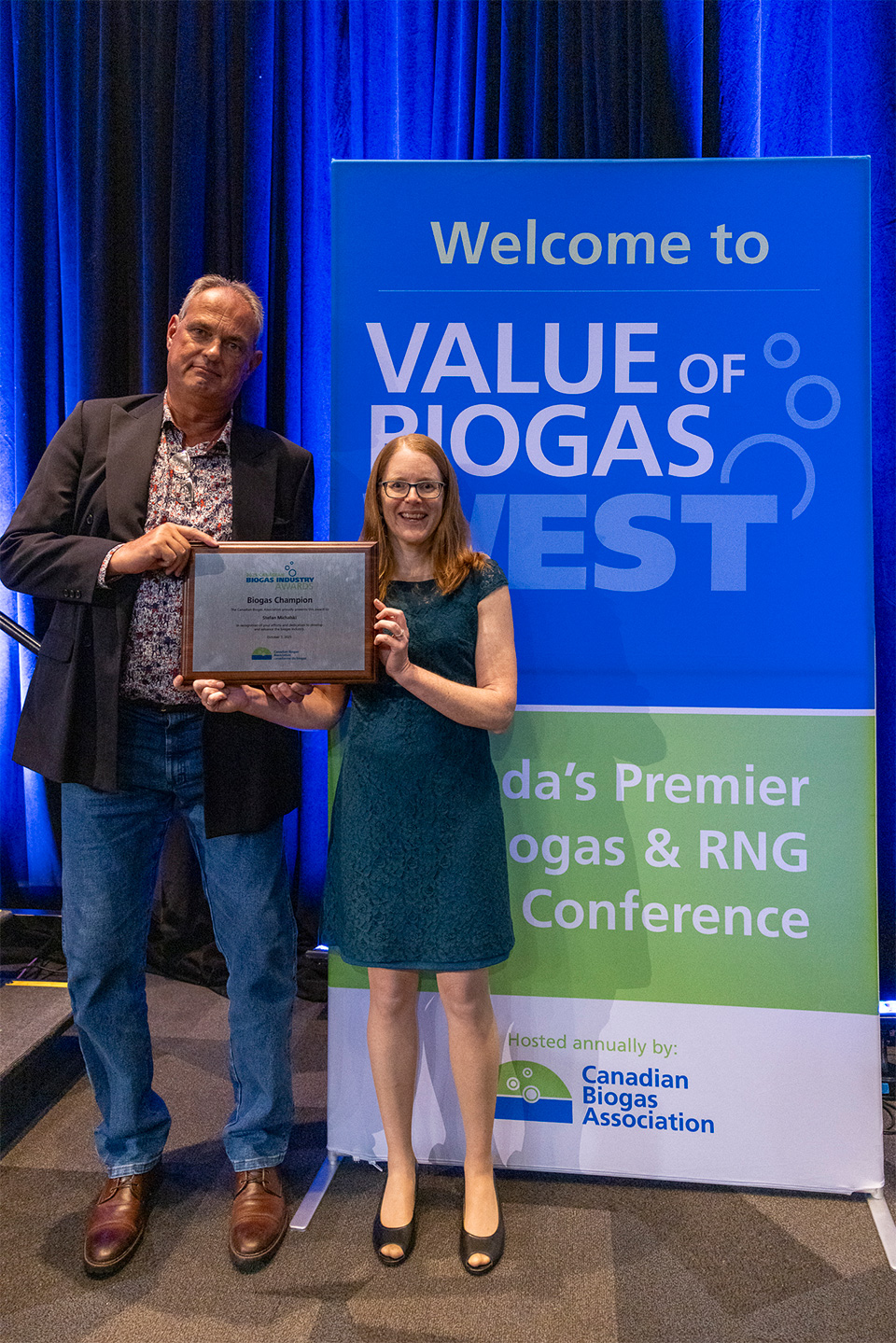 Jennifer Green standing next to Stefan Michalski, together they are holding a plaque with the award details inscribed.